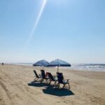Two beach chairs with umbrellas on a sunny sandy beach.