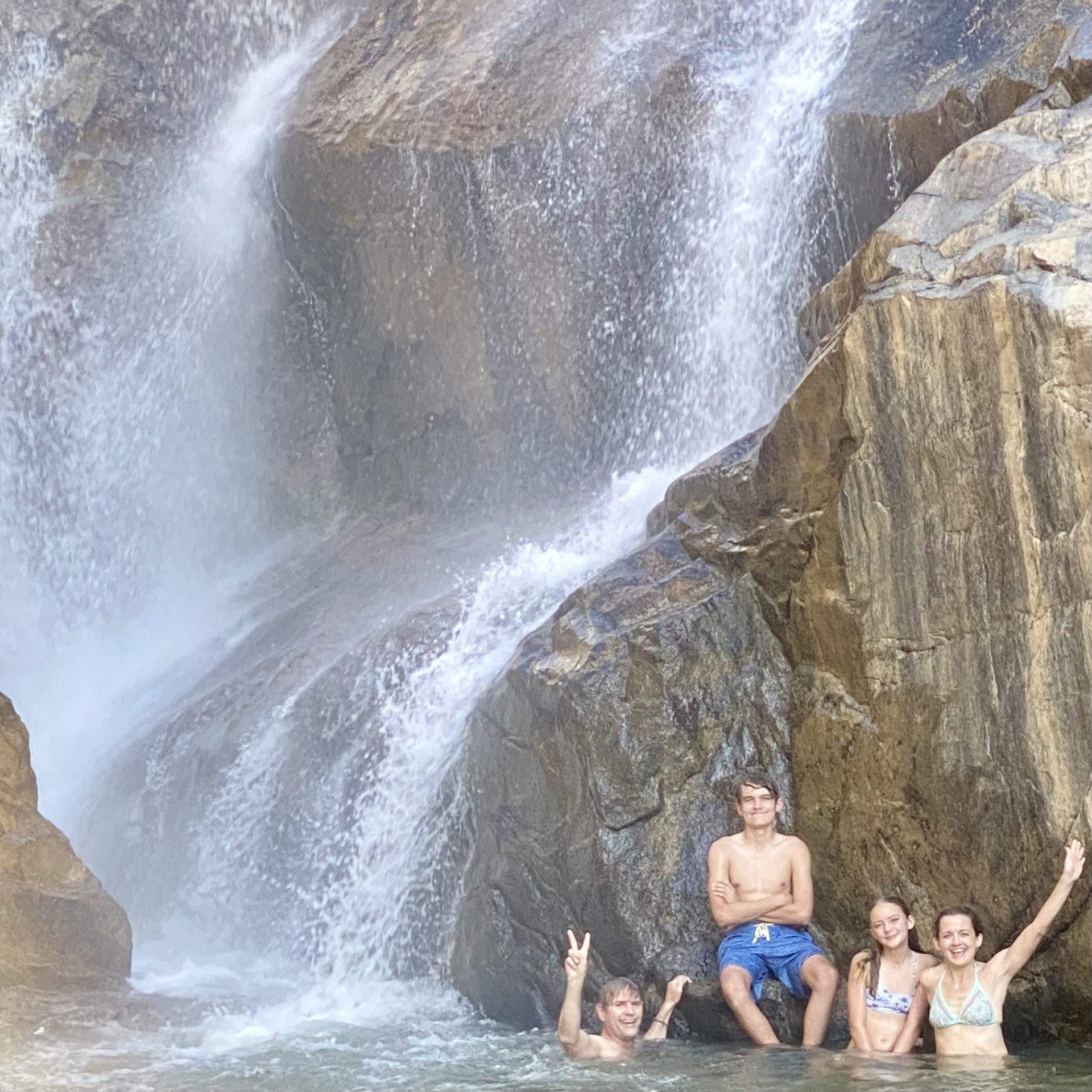 Four people enjoying a waterfall with rocky surroundings.