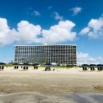A large beachfront hotel under a blue sky with scattered clouds.